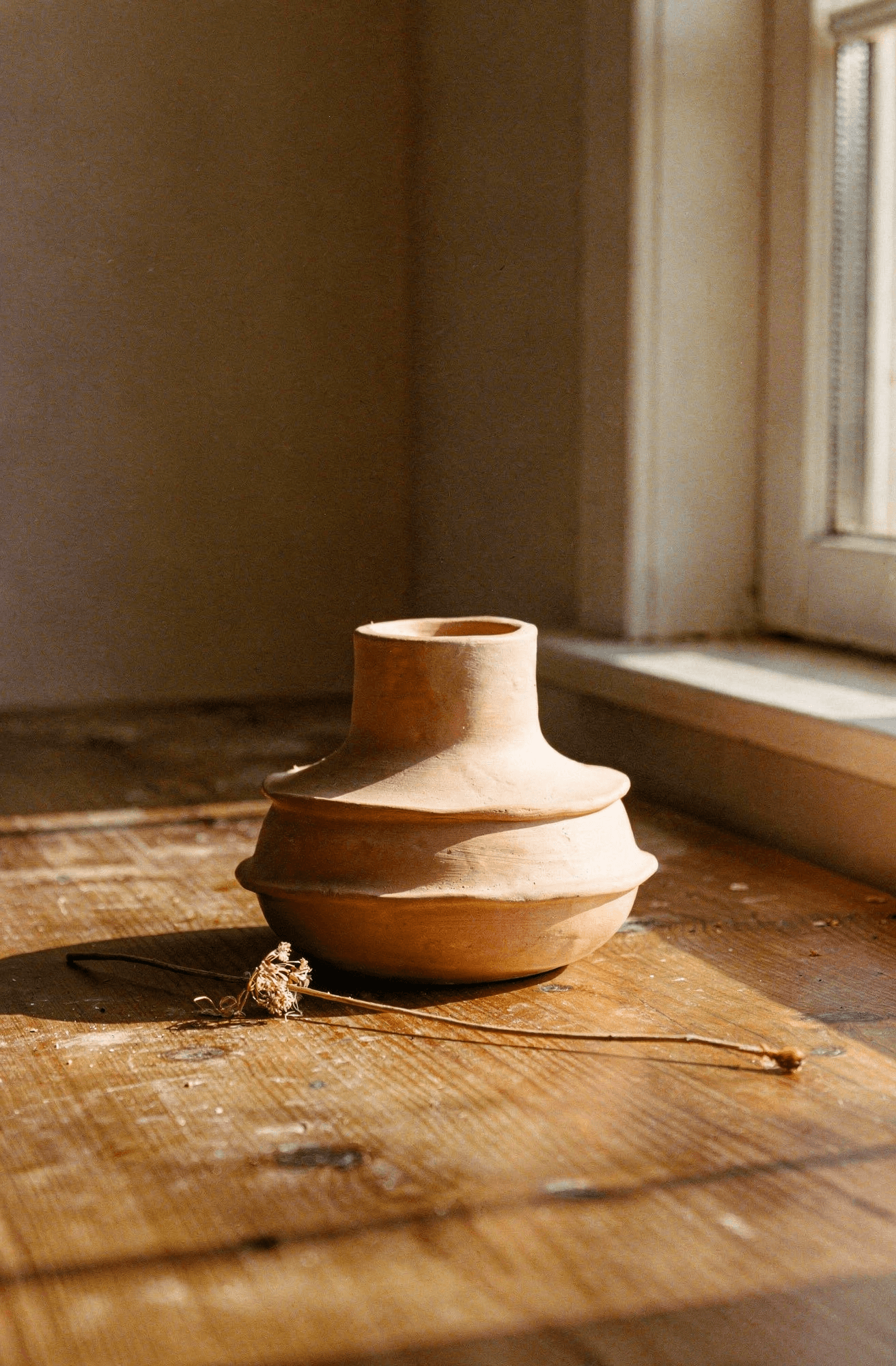 A terracotta clay vessel resting on warm wooden floorboards in afternoon light